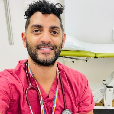 Photo of a handsome doctor wearing scrubs, looking to camera.