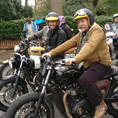 Photo of two men on classic motorcycles, smiling to camera.
