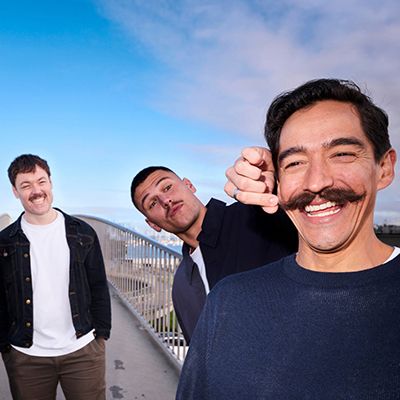 Photo of men with excellent moustaches, smiling to camera. One is twirling his friend's moustache