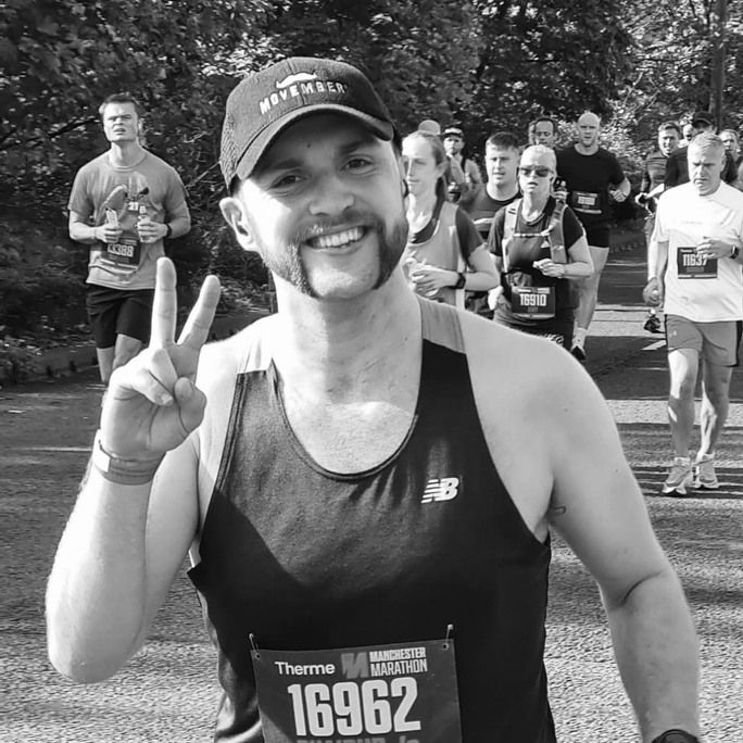 Black and white photo of athletic young man in running gear, smiling to camera.